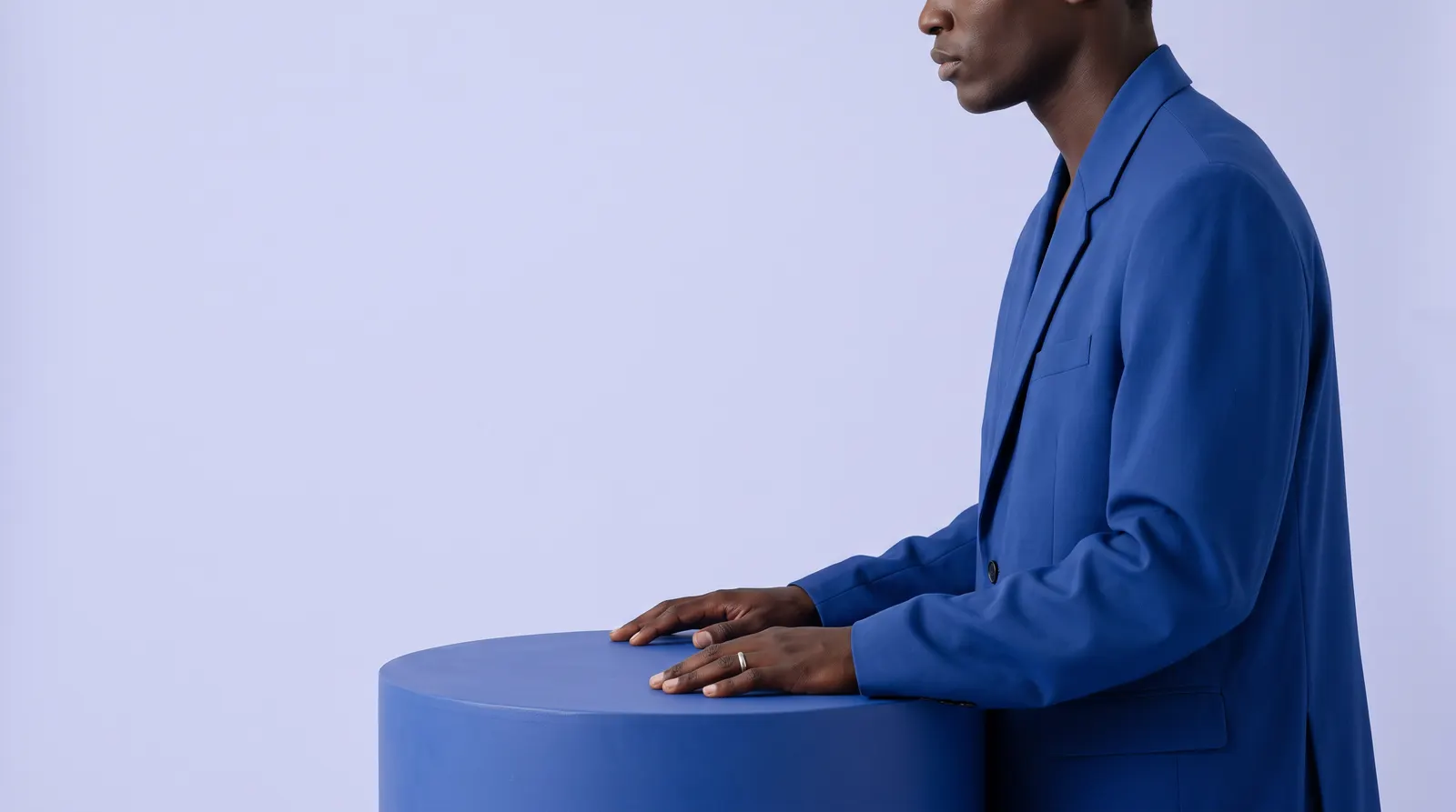 A Black South African man in a cobalt blue suit in profile, with both hands resting on a blue plinth