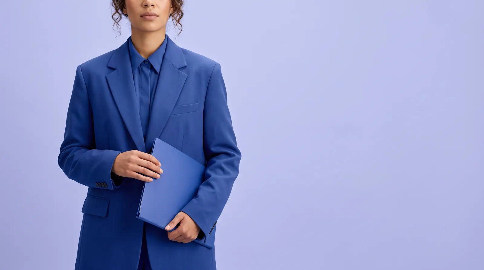 A coloured South African woman in a cobalt blue suit, holding a matte cobalt blue folder against her hip