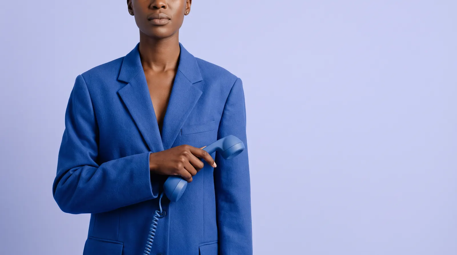 A Black South African woman in a cobalt blue suit, holding a telephone handset lowered away from her ear