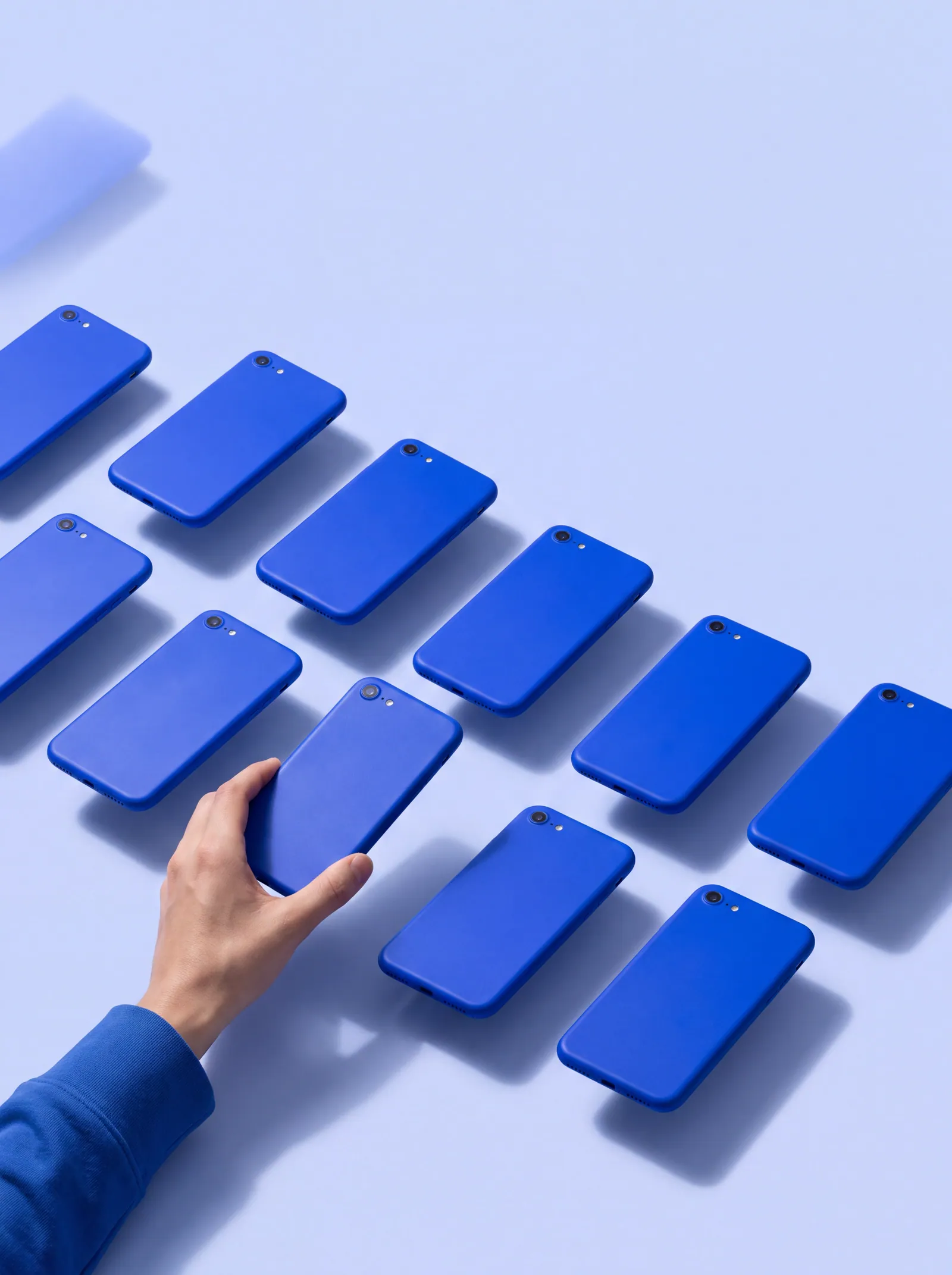 A grid of identical blue handsets on a pale blue surface, with one being lifted out by hand.